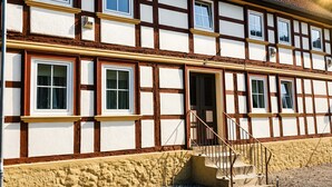 A traditional half-timbered building with multiple windows, a visible staircase, and a stone foundation. - Apartment 'Rehkitz' with Mountain View (Bad Lauterberg im Harz)