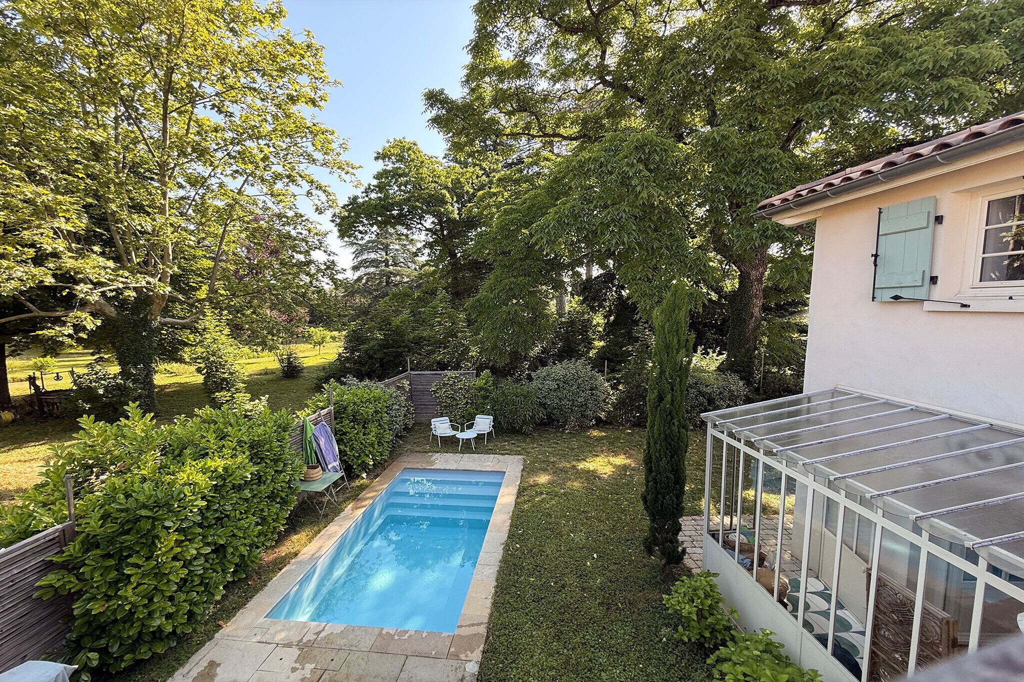 Ein Garten mit Swimmingpool, Gewächshaus und einer kleinen Terrasse mit Sitzgelegenheiten.