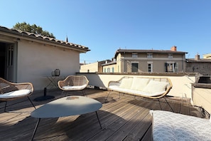 Eine Dachterrasse mit Korbmöbeln, einem Tisch und Blick auf umliegende Gebäude.