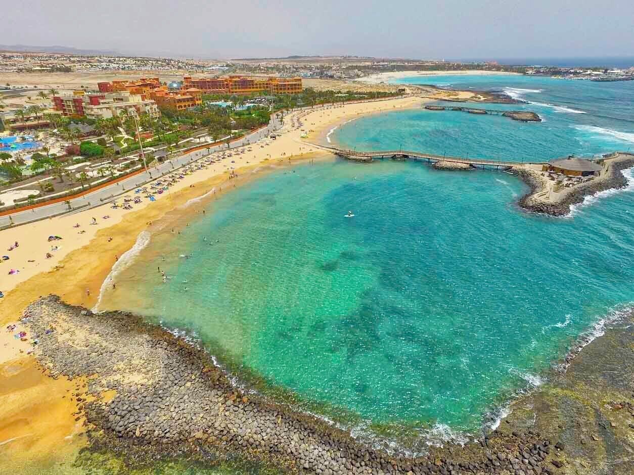 Una zona costiera con una spiaggia, un molo e un complesso alberghiero.