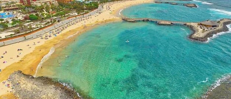 Una zona costiera con una spiaggia, un molo e un complesso alberghiero.