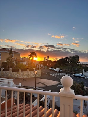Ein Sonnenuntergangsblick von einem Balkon mit einer Steinmauer, einer Straße mit Autos und einer Palme.