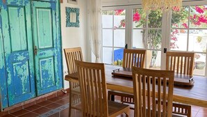 Een eetgedeelte met een houten tafel en stoelen, een blauwe deur met decoratieve snijwerken, en een hanglamp.