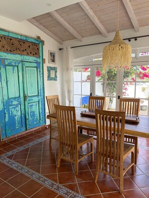 A dining area with a wooden table and chairs, a blue door with decorative carvings, and a hanging light fixture.