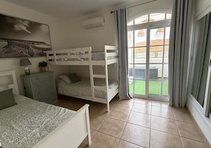 Ein Schlafzimmer mit Etagenbetten, einem Schreibtisch, einer Kommode und einem großen Fenster mit Vorhängen.