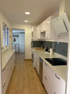 A modern kitchen with white cabinets, a built-in oven, a dishwasher, and a black induction cooktop.