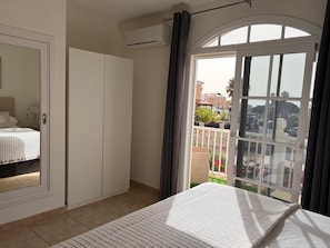 A bedroom with a bed, wardrobe, and a balcony with a view of the outside.