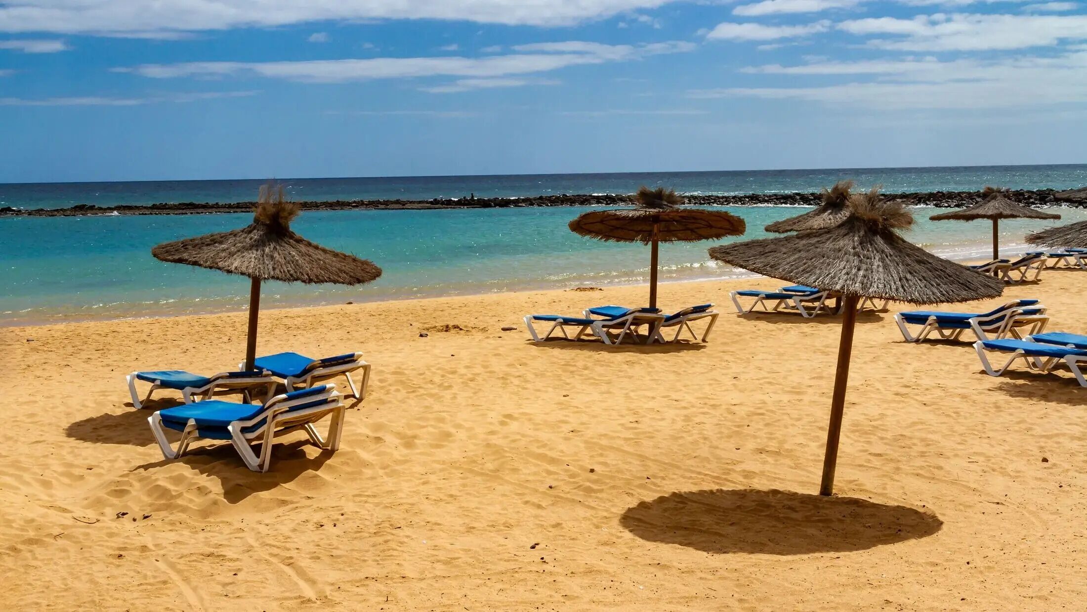 A beach with sun loungers and thatched umbrellas.
