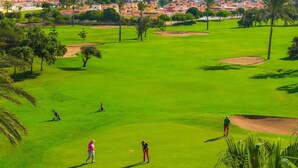 Een golfbaan met zicht op de green, zandbunkers en een veraf gelegen woongebied.