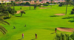 A golf course with a clear view of the green, sand bunkers, and a distant residential area.