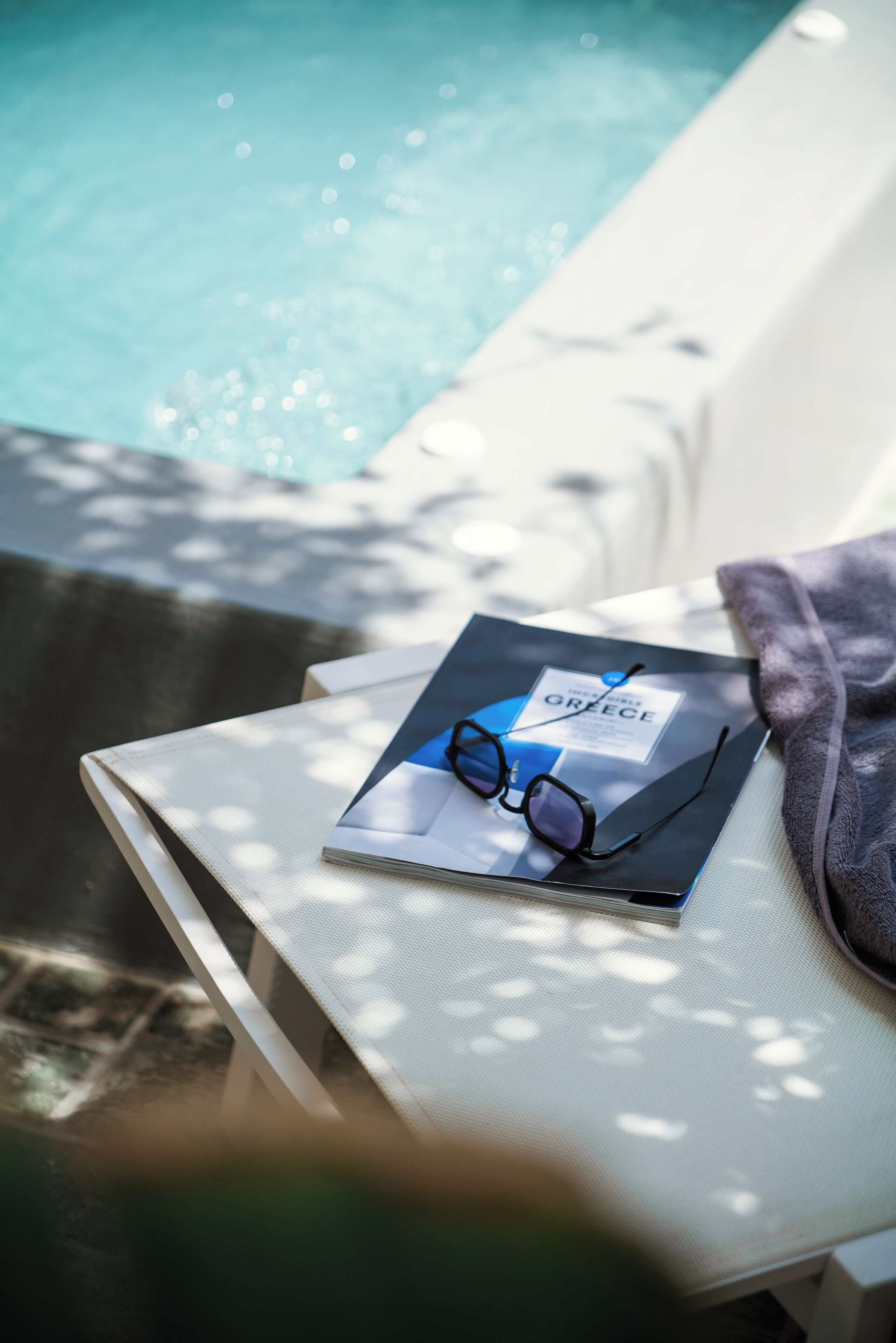 A poolside lounge chair with a book and glasses on it.