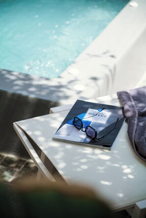 Eine Liege am Pool mit Buch und Brille darauf.