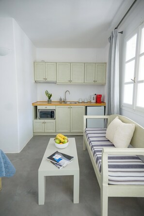Ein kompakter Wohnraum mit einer Küchenzeile, einem Esstisch mit einer Zeitschrift, einer Couch mit gestreiften Kissen und einem Fenster mit Vorhängen.