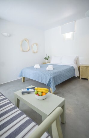 Ein schlicht eingerichtetes Schlafzimmer mit Bett, Nachttischen, einem kleinen Tisch mit Obst und einem Fenster.