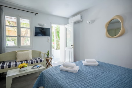 A room with a bed, a sofa, a small table with a bowl of fruit, and a TV on the wall.