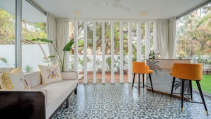 Habitación con sofá, dos sillones, una barra y ventanas grandes con cortinas.