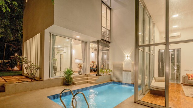 Una piscina interior moderna con paredes de vidrio, una zona de estar y una escalera que sube a un nivel superior.