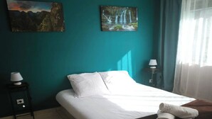 Un lit bien fait, avec du linge de lit blanc, une couverture en laine de couleur marron foncé et une serviette enroulée posée sur le lit. Deux lampes murales sont fixées de chaque côté du lit.