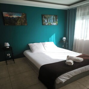 A bedroom with a bed, two wall-mounted lamps, a painting of a waterfall, and a window with curtains. - Villa Casa Kanden (Salazie)