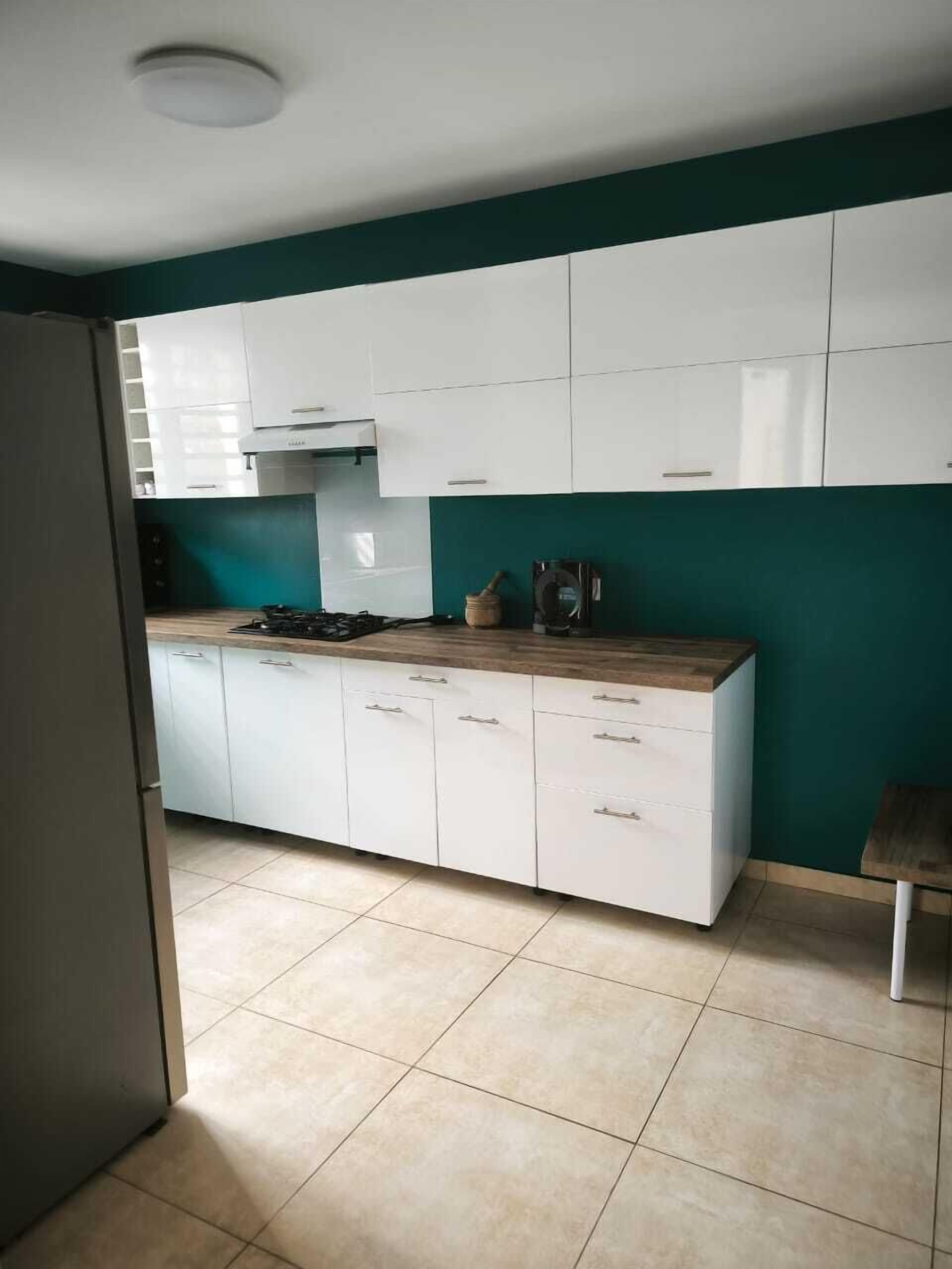 A modern kitchen with white cabinets, a wooden countertop, and a teal accent wall.