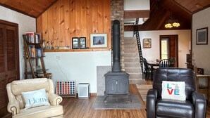 Un salon chaleureux avec une cheminée, des fauteuils en cuir, une bibliothèque et un escalier menant à un autre niveau.