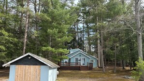 Une cabane dotée d’une terrasse en bois et d’un petit abri, entourée d’une forêt dense.