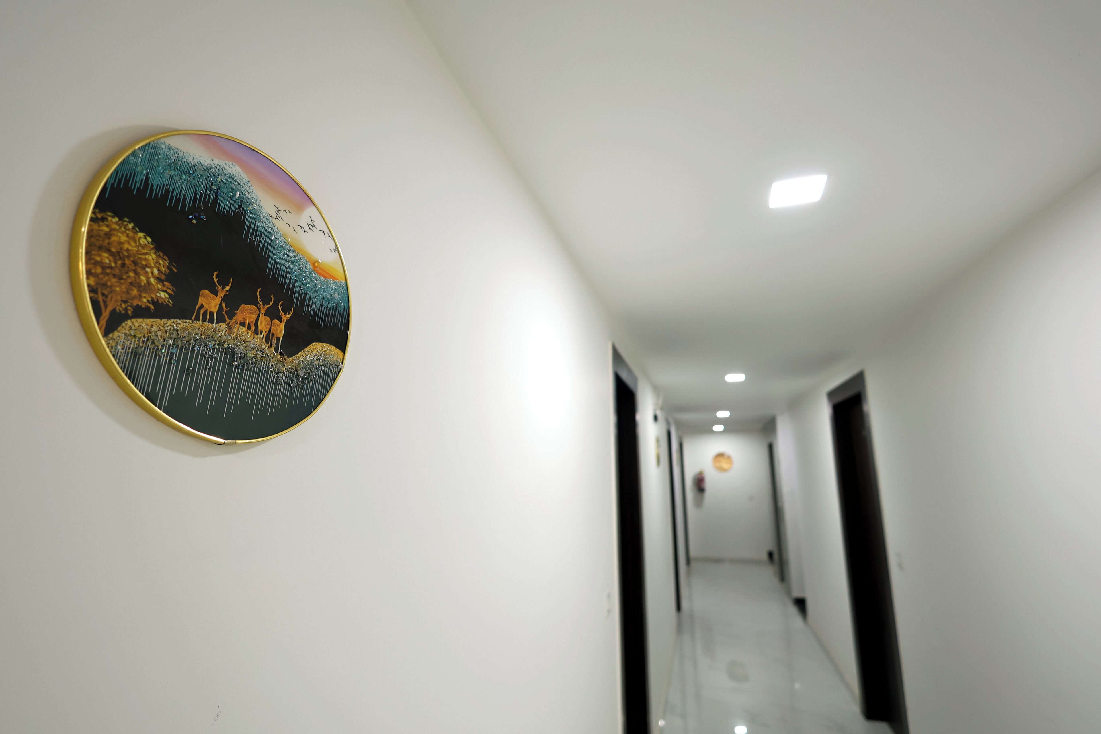 A hallway with a round, framed artwork on the left wall and a door at the end.