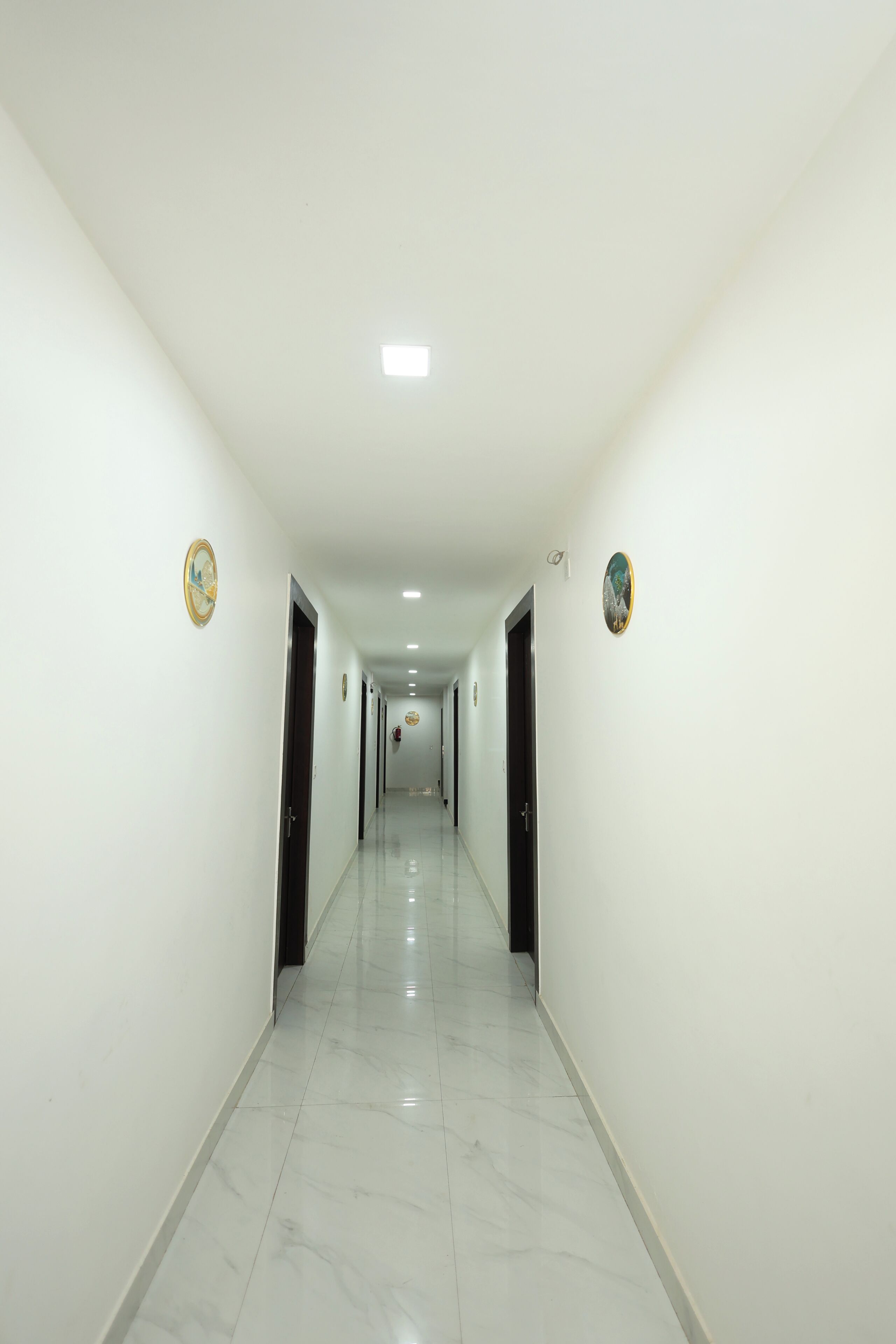 A long, narrow hallway with white walls and a shiny tiled floor, leading to multiple doors.