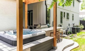 Ein Whirlpool unter einer Holzpergola, ein Grill und ein Garten mit Rasen und Zaun.