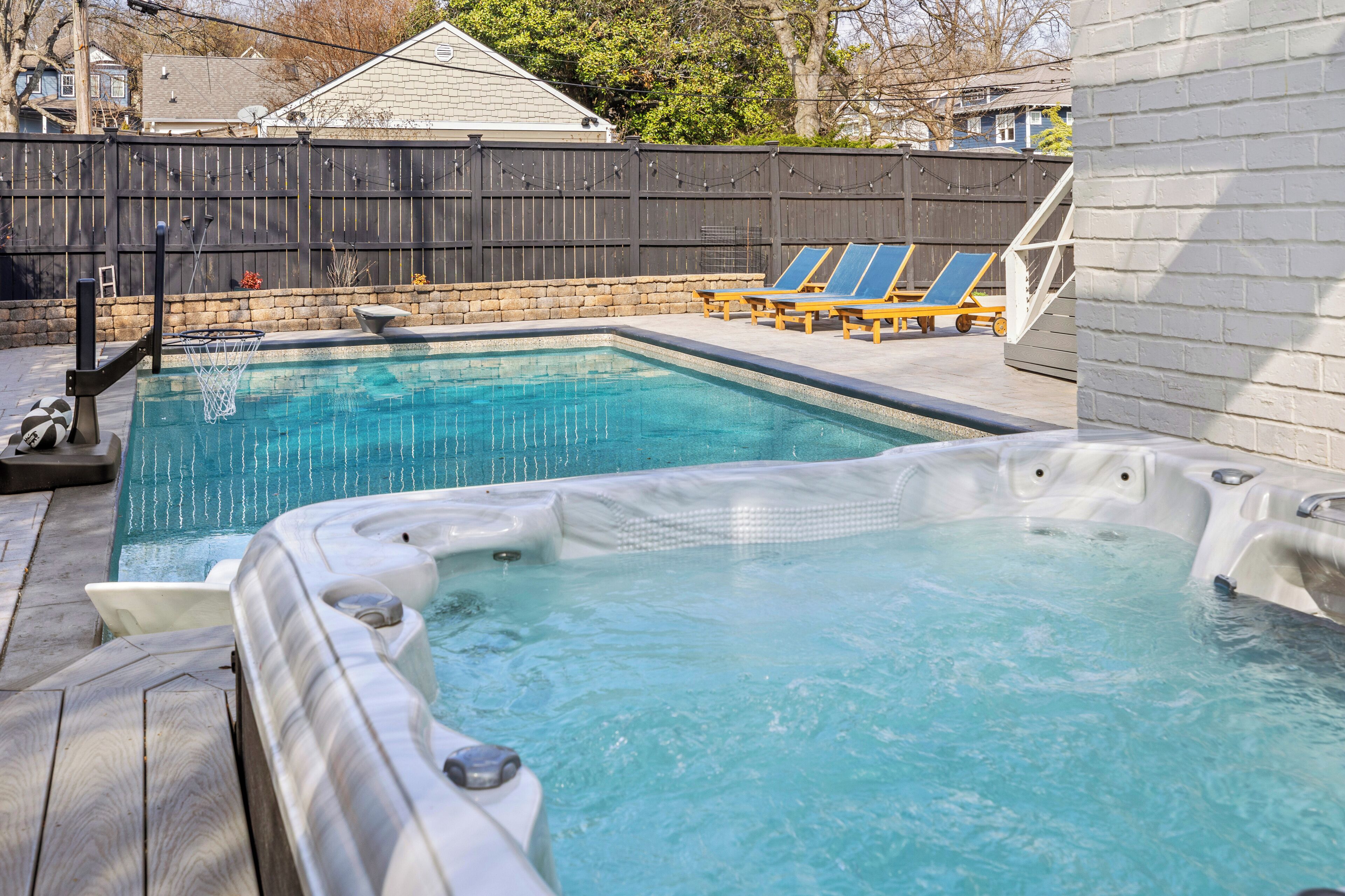 A swimming pool with a hot tub, lounge chairs, and a stone wall.
