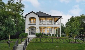 Ein zweistöckiges Haus mit einer Veranda, einer Treppe und einem eingezäunten Garten.