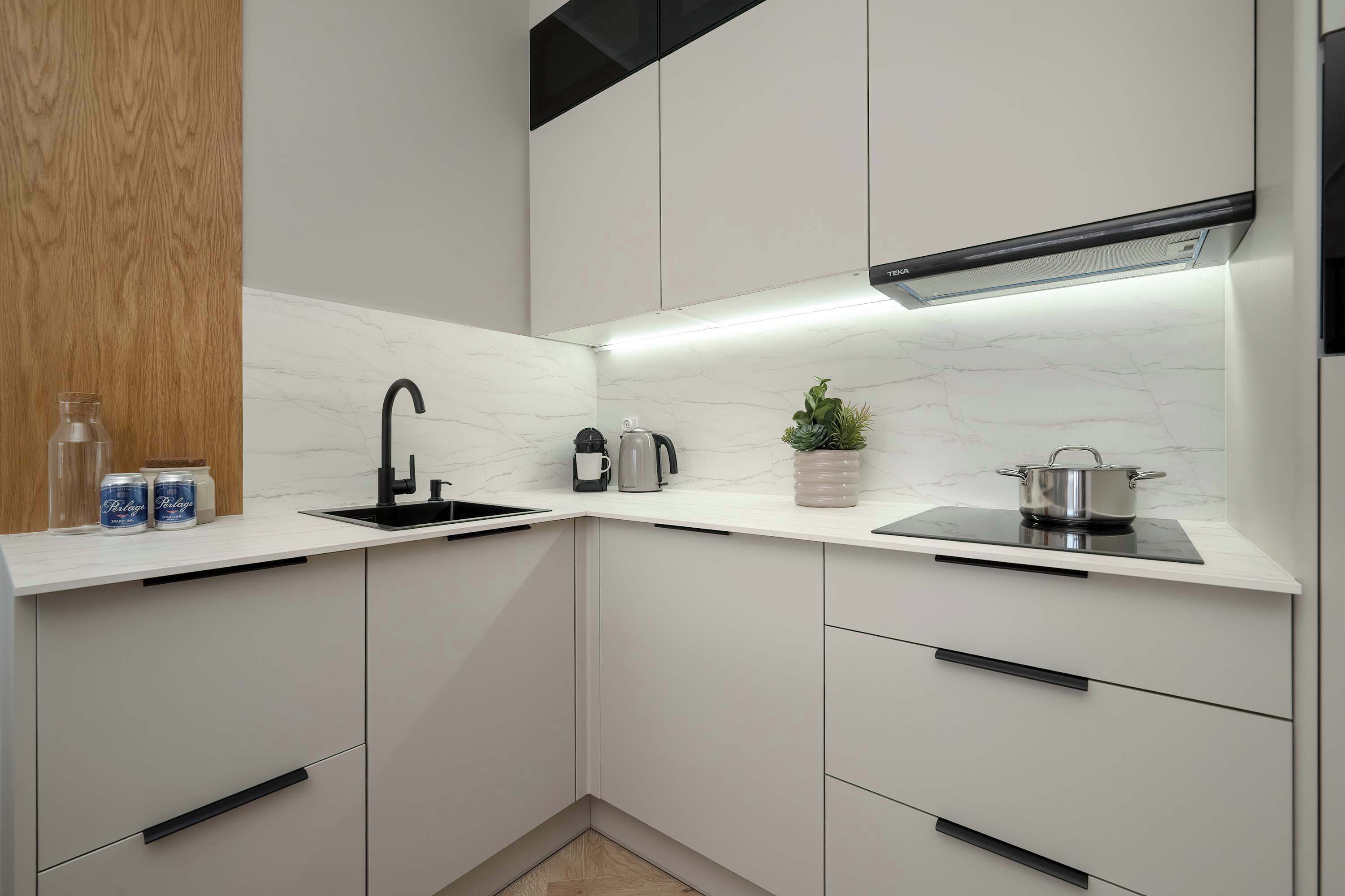 A modern kitchen with white cabinetry, a black faucet, a built-in stove, and a small potted plant.