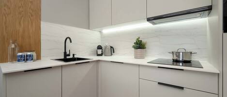 A modern kitchen with white cabinetry, a black faucet, a built-in stove, and a small potted plant.