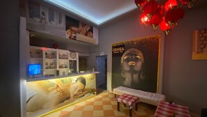 A hotel lobby with a reception desk, a check-in counter, a poster, a small table with a checkered tablecloth, and a patterned floor. - Cemsa Sunparadise BOUTİQUE HOTEL (Alanya)