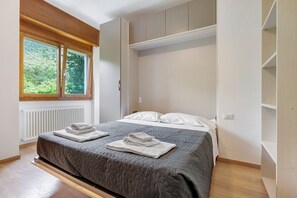 Une chambre Ă coucher avec un lit, deux fenĂȘtres, un radiateur et un plancher en bois.