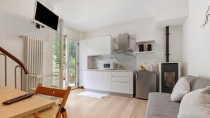 Eine moderne Küche mit weißen Schränken, einer eingebauten Mikrowelle und einem Herd. Es gibt einen Essbereich mit einem Holztisch und Stühlen sowie ein graues Sofa mit Kissen.