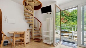 Ein Zimmer mit Schreibtisch aus Holz, einer Wendeltreppe, einem weißen Heizkörper und einer Glastür zum Außenbereich.