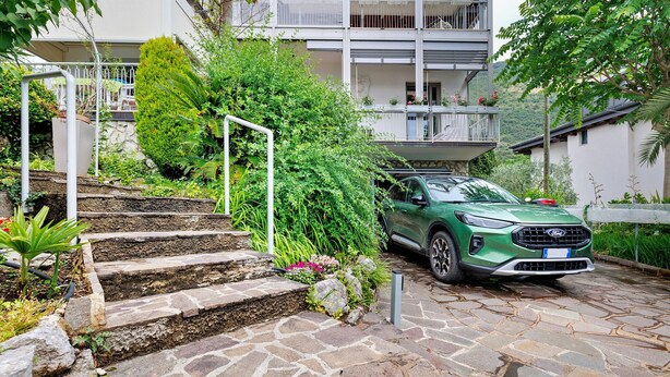 Ein grüner SUV auf einer Steintreppe, die zu einem Gebäude mit Balkonen führt.