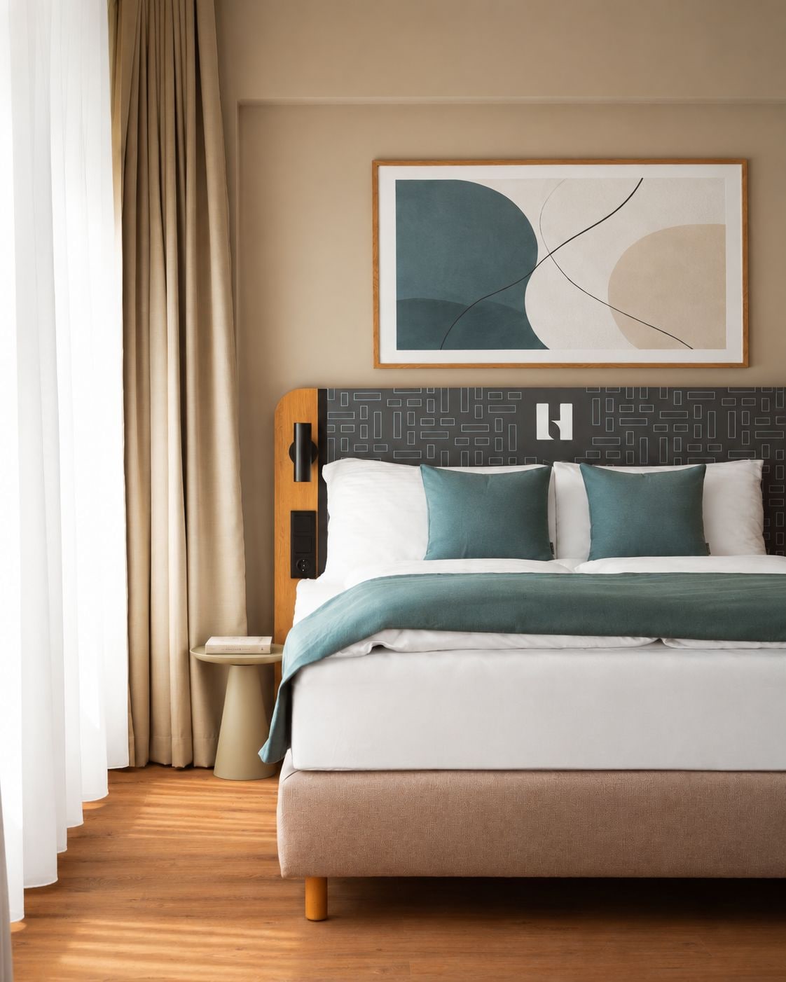 A hotel room with a bed, a bedside table, a wall-mounted artwork, and a window with curtains.
