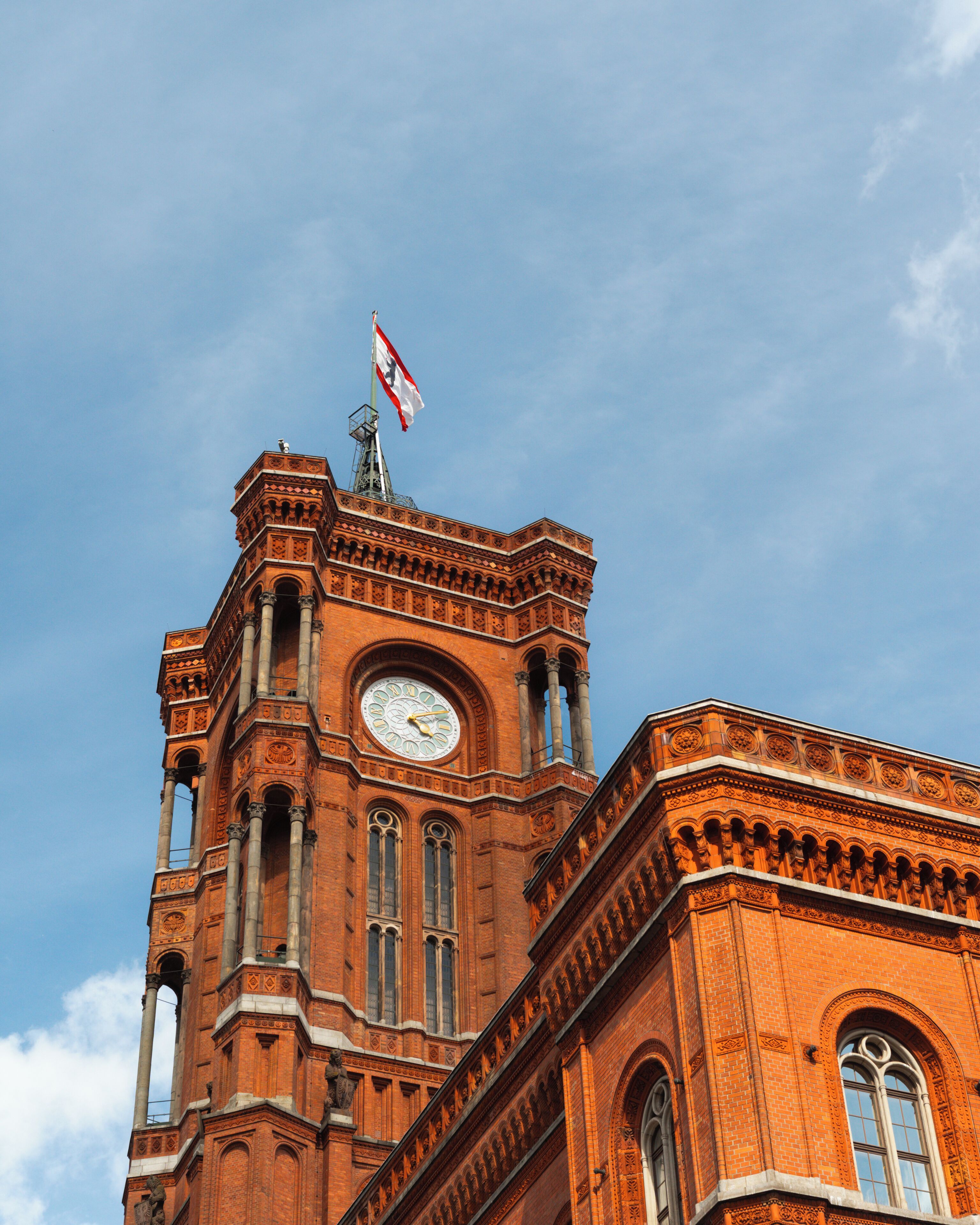 A historic building with a clock tower, arched windows, and a flag.
