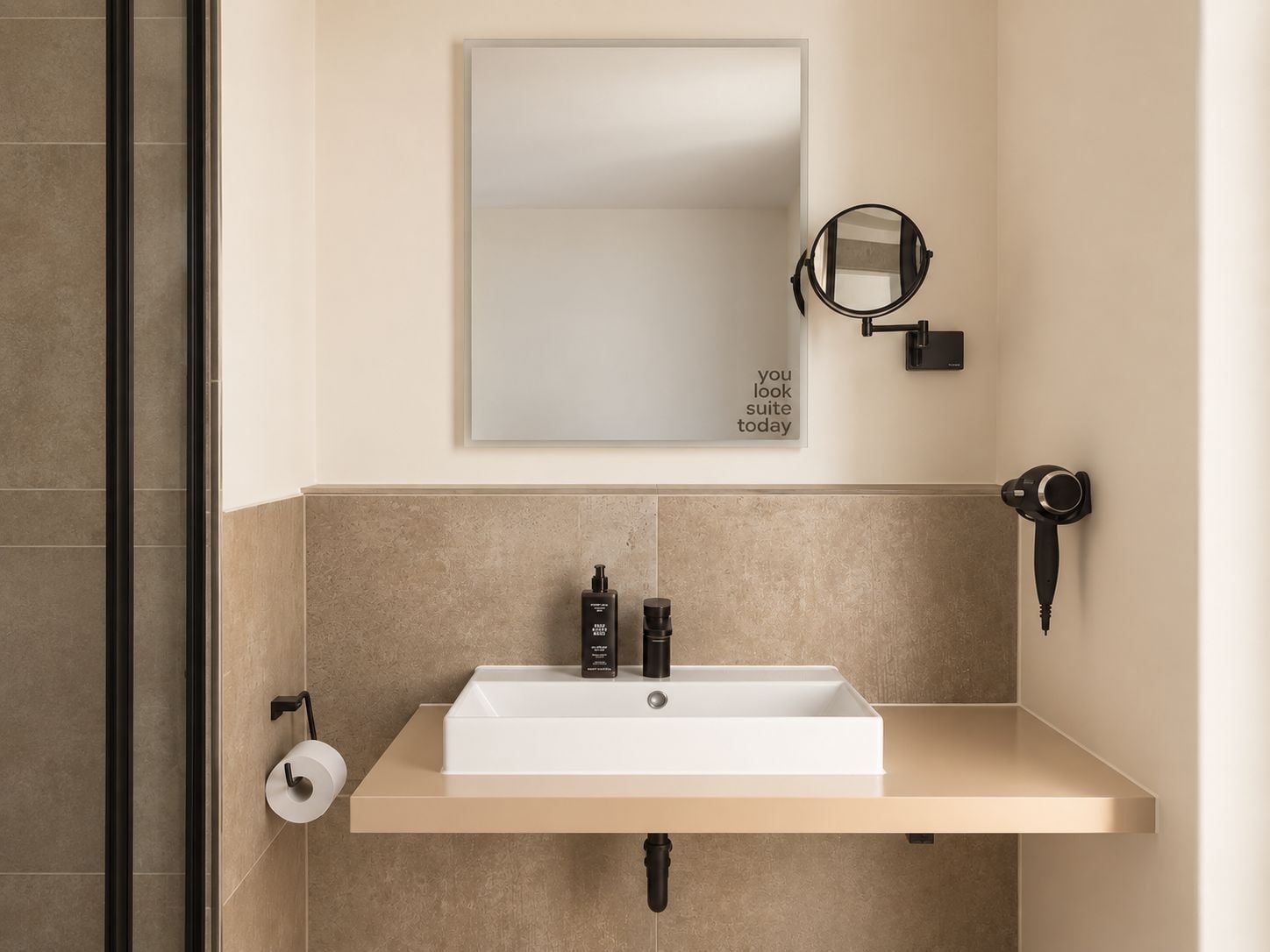 Un baño con lavamanos blanco, un espejo, dispensador de toallas y secador de pelo.