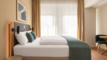 Una habitación de hotel con cama, mesita de noche, una silla y una ventana con cortinas.