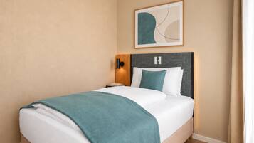 Habitación de hotel con cama, mesita de noche, lámpara de pared y una obra de arte abstracta enmarcada.