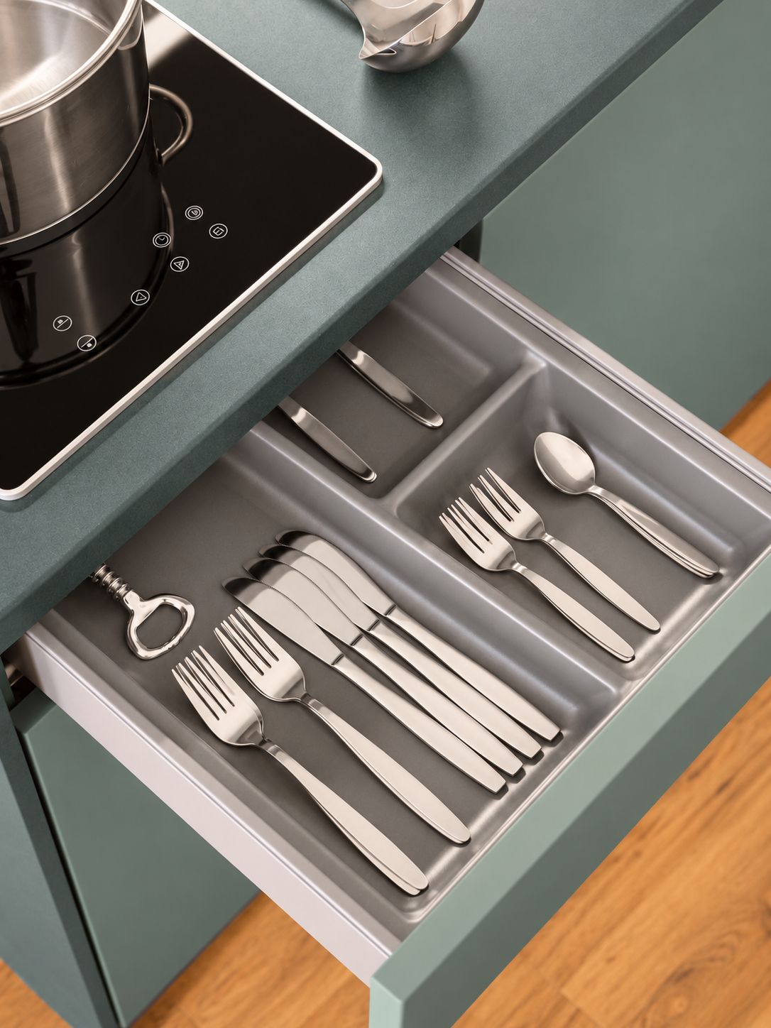 Un tiroir de cuisine contenant des ustensiles et une casserole sur une plaque de cuisson à induction.