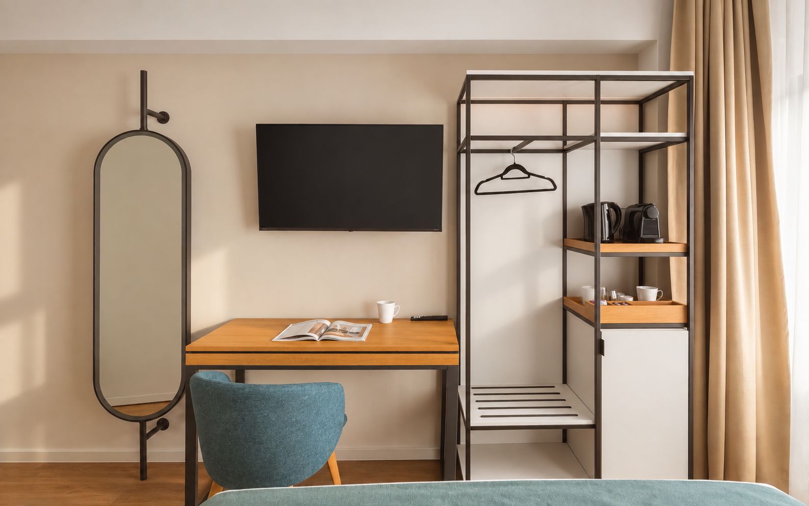 Una habitación compacta con un escritorio de madera, una silla azul, un espejo con marco negro, un televisor negro y una estantería metálica con perchero.