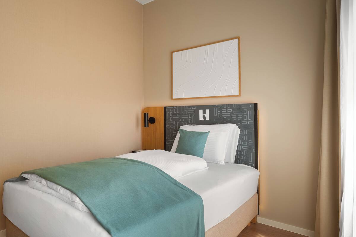 Una cama bien hecha con una manta verde, un cabecero con un diseño geométrico y una obra de arte enmarcada encima.