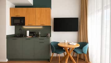 A modern kitchen with a flat-screen TV, a dining table with chairs, and a large window with curtains.