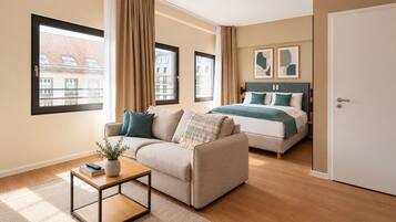 A modern bedroom with a bed, a sofa, a coffee table, and a view of buildings through the window.