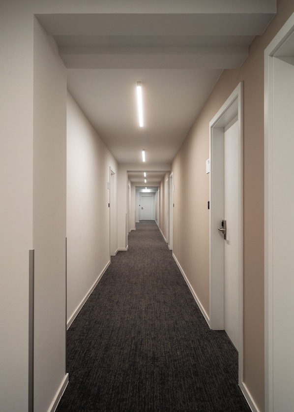 A long, narrow hallway with carpeted floors and white walls, leading to multiple doors. - Limehome Berlin Klosterstraße (Berlin)
