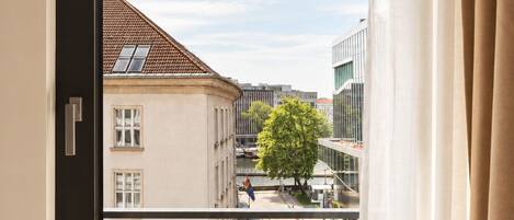 Une fenêtre donnant sur un bâtiment avec un toit recouvert de tuiles et un arbre au premier plan.